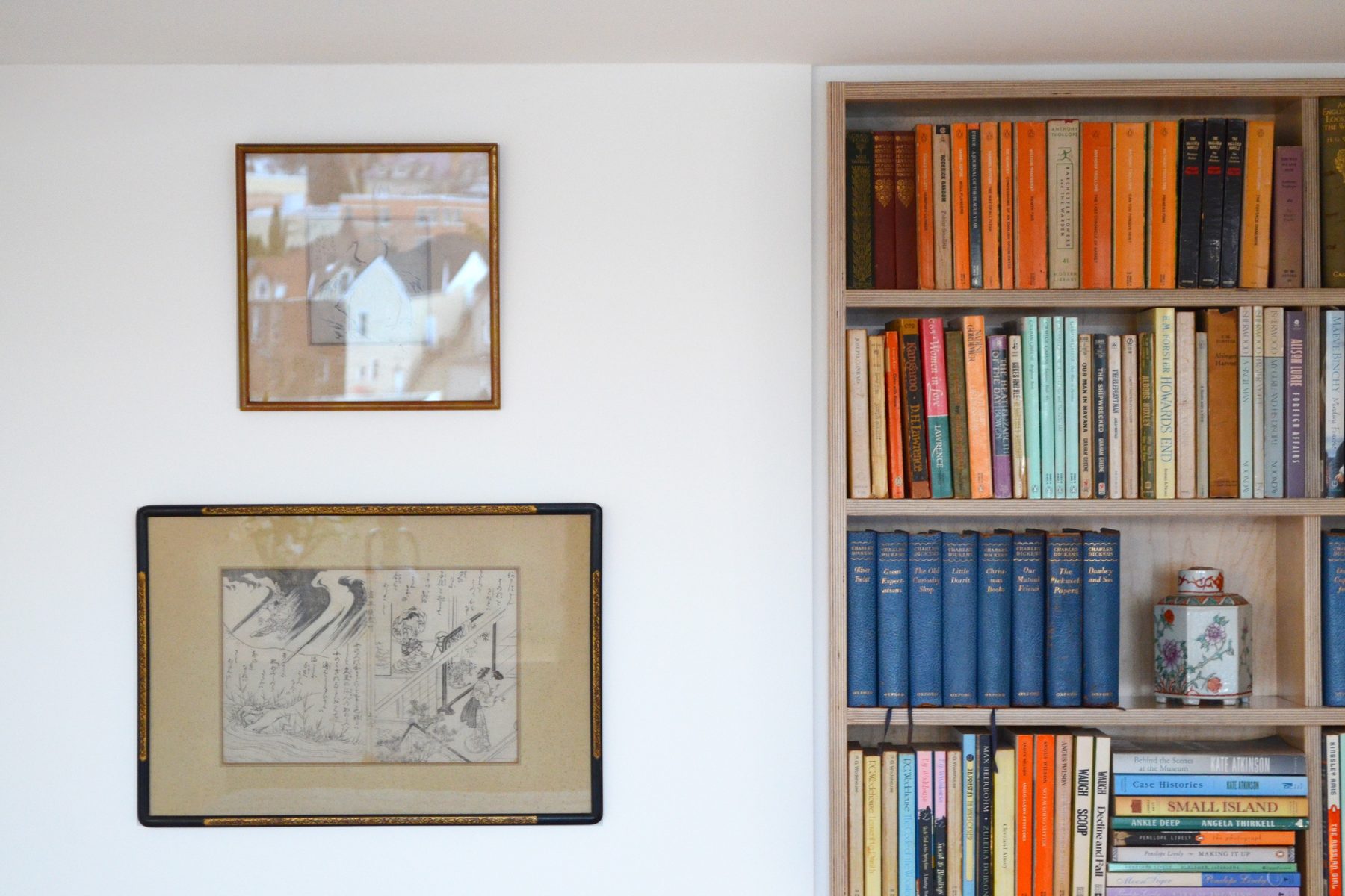 A living-room wall of framed prints beside a bookcase filled with coloured spines